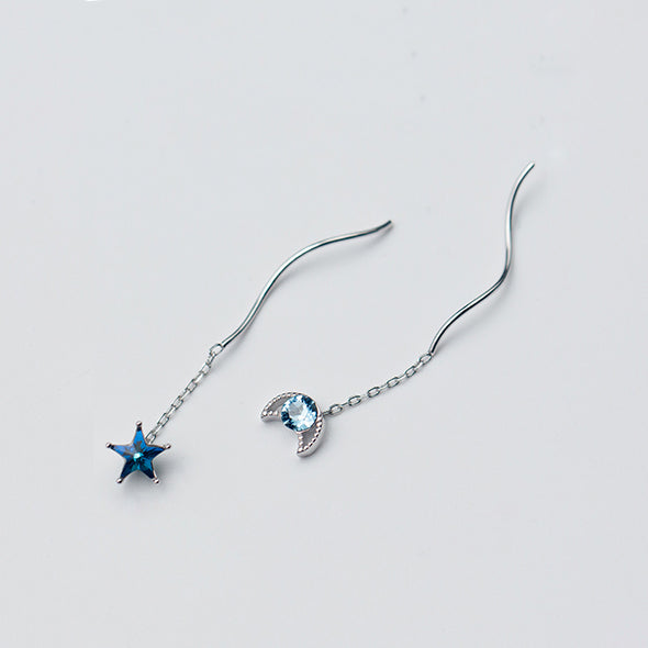 Une paire de boucles d'oreilles pendantes dépareillées en argent 925 avec une étoile et une lune, ornées de diamants de zirconium bleu saphir.