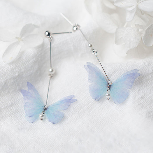 Boucles d'oreilles pendantes longues avec papillon et perle - Argent 925. Un papillon aux nuances bleutées et violettes vole au-dessus d'une perle élégante. Un bijou poétique et élégant pour chaque femme.