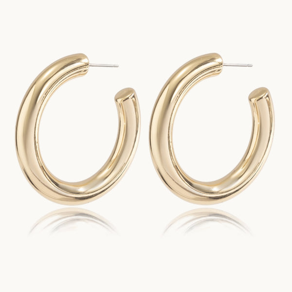 Une paire de boucles d'oreilles est exposée devant un fond beige.  Ce sont des créoles rondes et épaisses dorées.