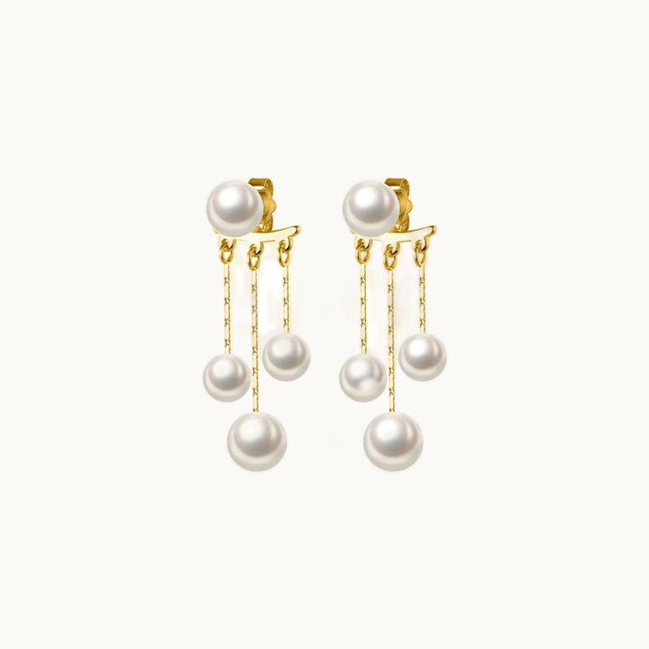 Une paire de boucles d'oreilles est exposée devant un fond beige.  Ce sont des boucles pendantes. Il y a une perle sur le haut et il y a trois chaînes qui pendent sur lesquelles pend une perle. Elles sont en argent 925 plaqué or.