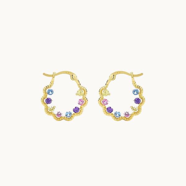 Une paire de boucles d'oreilles est exposée devant un fond beige.  Ce sont des créoles torsadées avec des strass colorés en forme de goutte à l'intérieur.