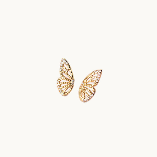 Une paire de boucles d'oreilles est exposée devant un fond beige.  Ce sont des papillons de profil avec strass. Les boucles sont en plaqué or. 