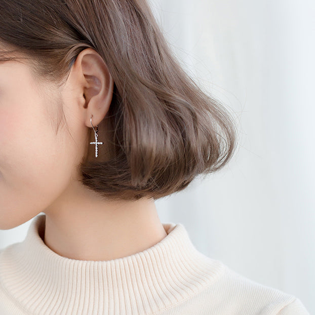 Femme portant des boucles d'oreille dormeuses croix pendante strass en argent 925 - Élégance intemporelle pour ajouter une touche de brillance à votre tenue.
