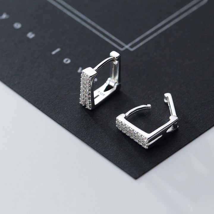 Une paire de boucles d'oreille créoles rectangulaires en argent 925 avec des strass étincelants, ajoutant une luminosité sophistiquée et contemporaine. Un design audacieux et un éclat inimitable pour impressionner.