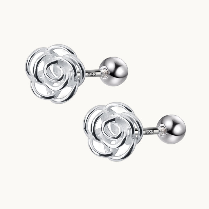 Une paire de boucles d'oreilles est exposée devant un fond beige.  Ce sont des roses en argent. 