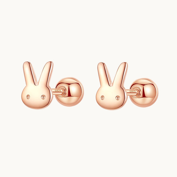 Une paire de boucles d'oreille est exposée devant un fond beige.  Ce sont des boucles en forme de tête de lapin mignonne. Les boucle sont en argent 925 plaqué or rose. 