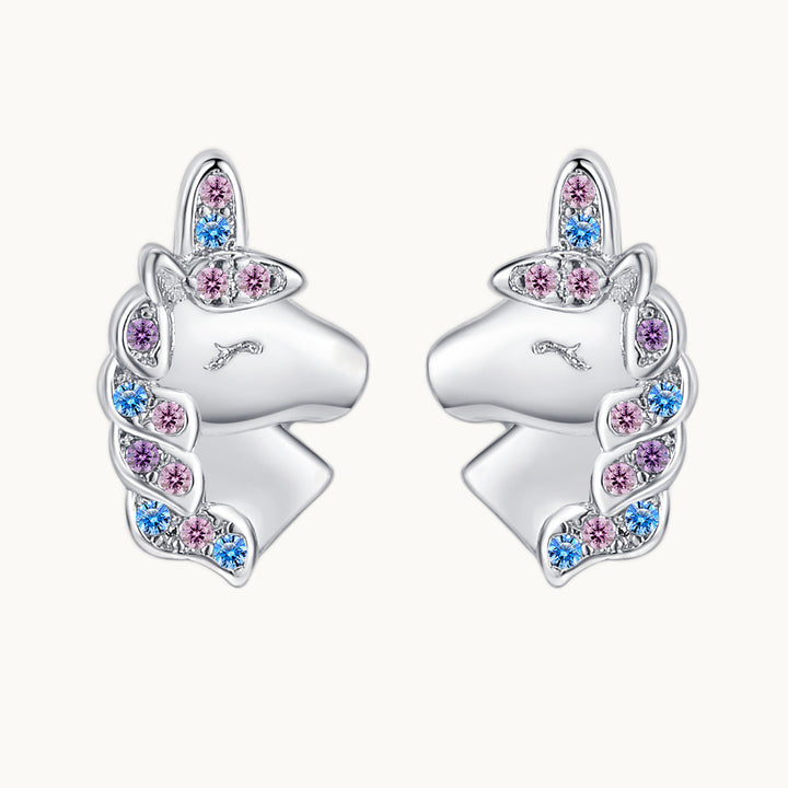 Une paire de boucles d'oreilles est exposée devant un fond beige.  Ce sont des boucles d'oreille en forme de licorne. La crinière et la corne sont en strass de couleur pastel (rose, bleu, violet.) Elles sont en argent 925.
