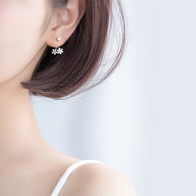 Une femme porte une robe blanche et des boucles d'oreille pendantes en argent 925 avec des strass scintillants et des fleurs blanches et diamants. Parfaites pour une soirée ou pour sublimer votre look quotidien, ces boucles d'oreille capturent la beauté et la délicatesse des fleurs.