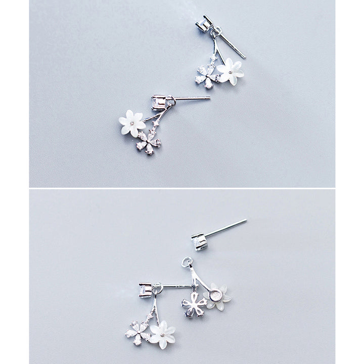 Une paire de boucles d'oreille pendantes en argent 925 avec des fleurs et des diamants. Un strass scintillant pend délicatement d'une fleur blanche immaculée et d'une autre ornée de pétales en diamant. Un choix élégant pour sublimer votre look quotidien ou illuminer une tenue de soirée.