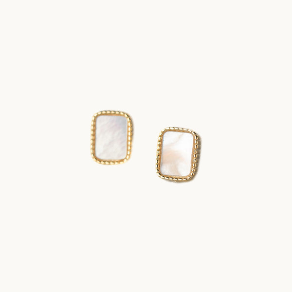 Une paire de boucles d'oreilles est exposée devant un fond beige.  Ce sont des boucles rectangulaires en argent 925 plaqué or. Elles sont nacrées. Elles ont un look rétro. 