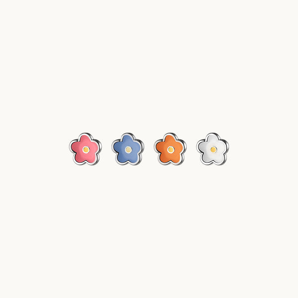 4 boucles d'oreilles fleur colorée et argent sont exposées sur un fond beige. Il y en a une rose, une bleue, une orange et une blanche. 