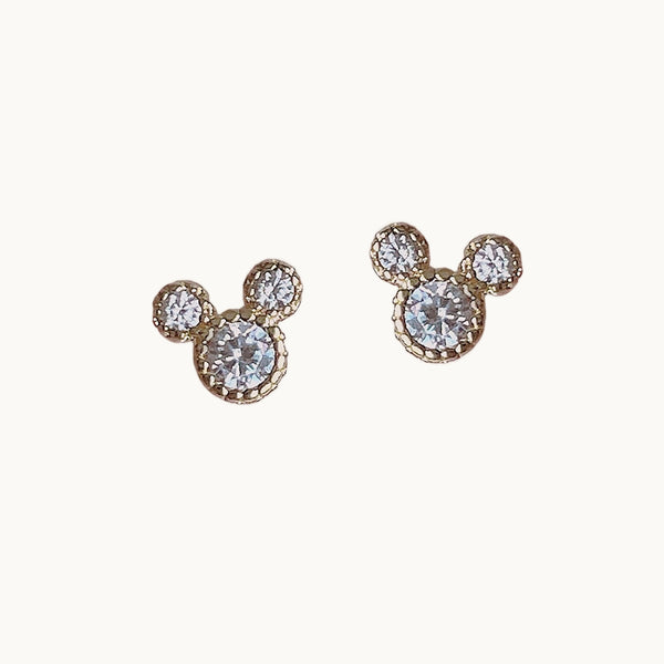 Une paire de boucles d'oreilles est exposée devant un fond beige.  Ce sont des boucles d'oreille strass en forme d'ourson dorées.