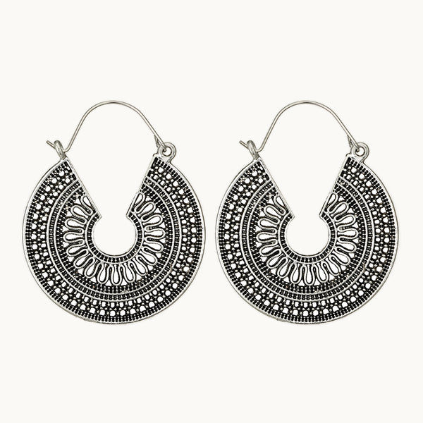 Une paire de boucles d'oreilles est exposée devant un fond beige.  Ce sont des boucles d'oreilles rondes en argent bohème et ethnique. 