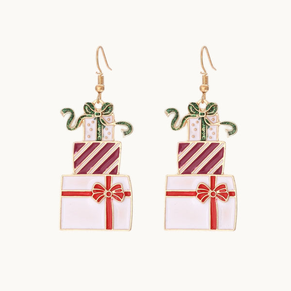 Une paire de boucles d'oreille est exposée devant un fond beige.  Ce sont des boucles d'oreille en forme de paquets cadeaux colorés dans les tons de blanc, verts et rouges. Elles sont idéales pour les fêtes de noël. Elles sont dorées.