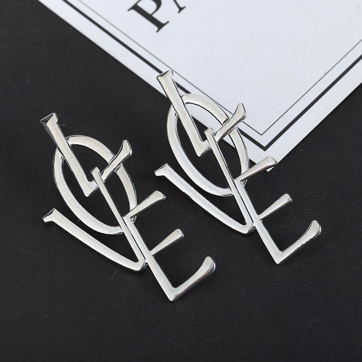 Boucle d'oreille longue oversize représentant le mot "LOVE" en lettres enchevêtrées en alliage de zinc argenté et doré pour femme. Design moderne et tendance.