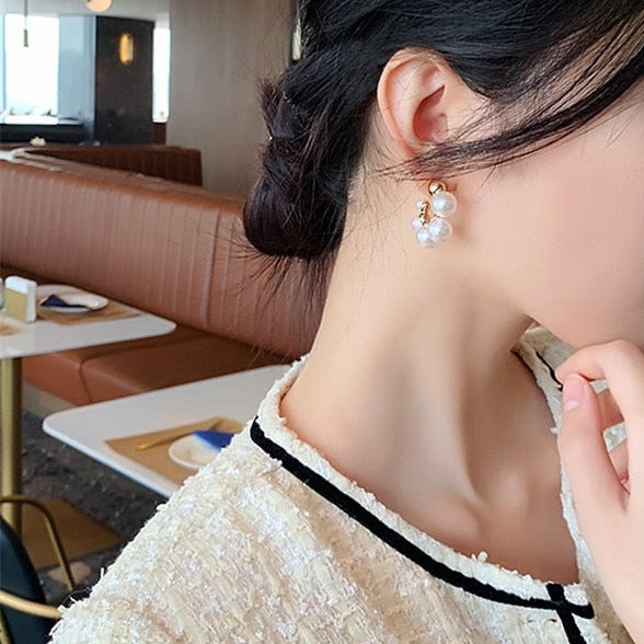 Une femme portant une chemise blanche et des boucles d'oreilles créoles dorées avec perles. Un bijou sophistiqué et élégant pour ajouter du caractère à n'importe quelle tenue.