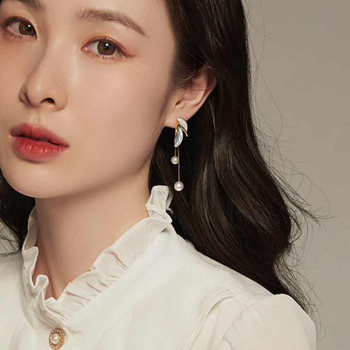 Une femme avec de longs cheveux portant un chemisier blanc et des boucles d'oreille pendantes en perles et strass.