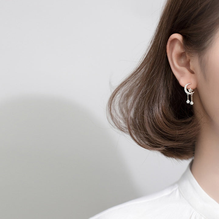 Une femme porte des boucles d'oreille en forme de lune avec une étoile scintillante, des diamants de zirconium pendants ajoutent une touche d'éclat et de mouvement. Boucle d'oreille lune strass étoile diamants pendants - Femme - Argent 925.