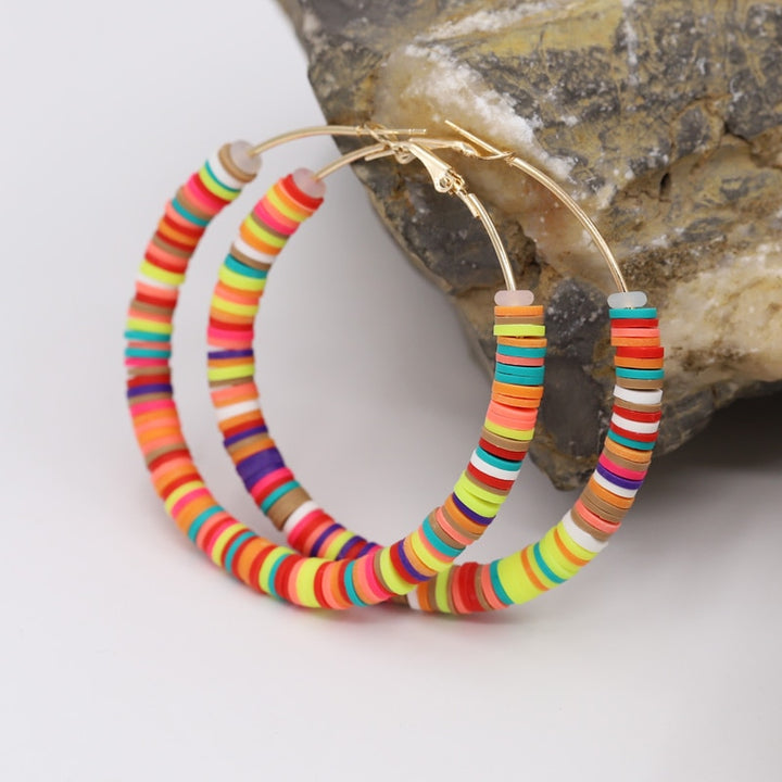 Boucle d'oreille créole anneaux plats colorés argile - Enfant: une paire de boucles d'oreille créoles dorées avec de multiples petits anneaux plats en argile aux couleurs vives. Parfait mélange entre amusement et élégance pour votre petite fille. Dimensions: 65 x 65 mm. Poids: 12,5 g.