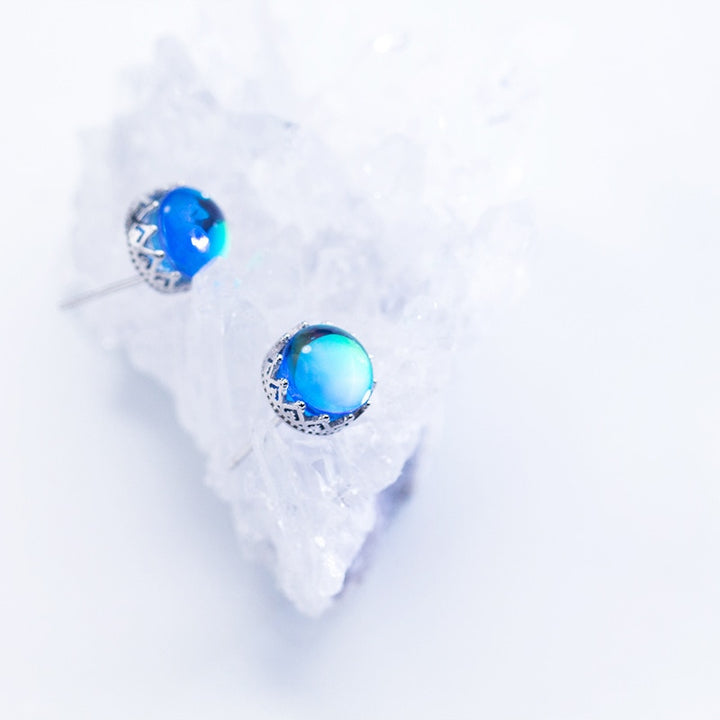 Une paire de boucles d'oreilles en forme de couronne avec un cristal bleu rond irradie des reflets arc-en-ciel - Femme - Argent 925.