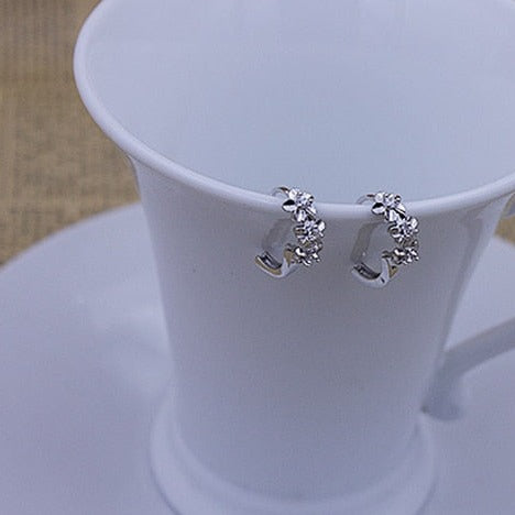 Boucle d'oreille créole fleurs strass - Femme - Argent 925, dans une tasse blanche en céramique. Trois fleurs scintillantes ornent chaque boucle, avec un strass étincelant en leur cœur. Une élégance inégalée pour chaque femme.