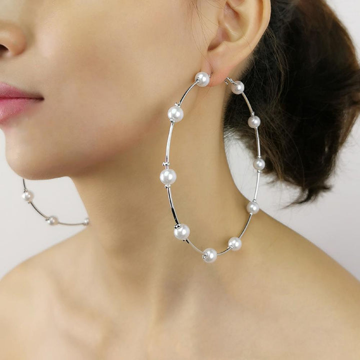 Une femme porte des boucles d'oreille grandes créoles avec des perles rondes, ajoutant une élégance intemporelle à sa tenue. Les boucles d'oreille sont en alliage de fer et perles artificielles, disponibles en couleur or ou argent. Un accessoire féminin séduisant et raffiné de la collection de boucles d'oreille de 1001 Boucles d'Oreille.