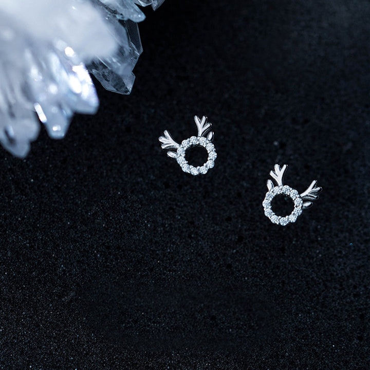 Une paire de boucles d'oreille rondes argentées avec des cristaux scintillants représentant la tête d'un renne joyeux. Parfaites pour les festivités de Noël.