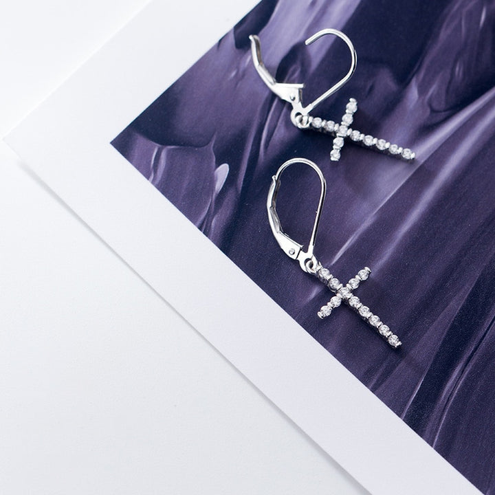 Une paire de boucles d'oreille dormeuses en argent 925 avec une croix pendante ornée de strass scintillants. Un mélange harmonieux de tradition et de modernité pour ajouter une touche de brillance à votre tenue.