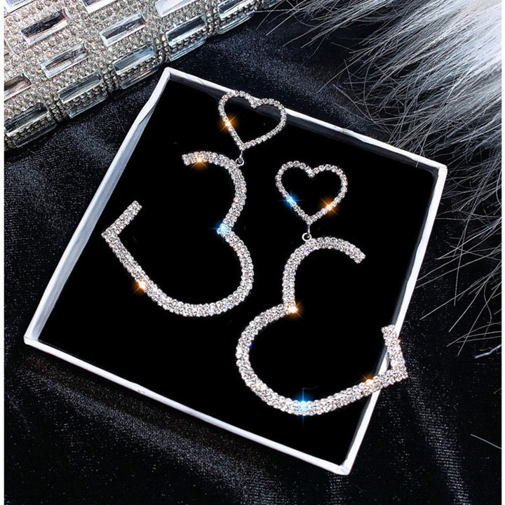 Une paire de boucles d'oreille créoles avec des cœurs en strass - Femme. Ajoutez de l'éclat et de la romance à votre look avec ces boucles d'oreille délicates en argent ou en or.