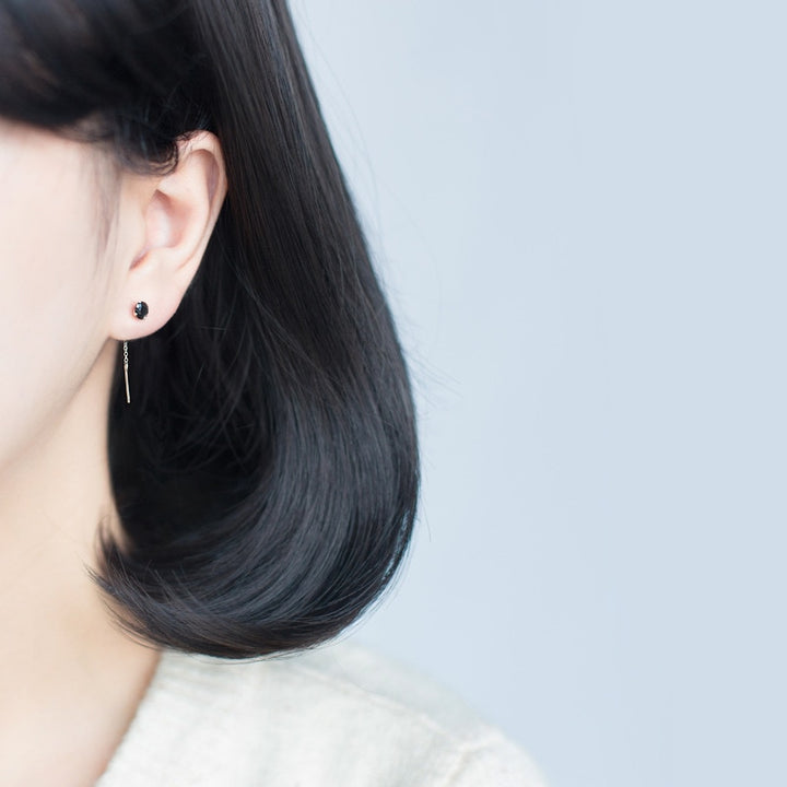 Une femme avec des cheveux noirs portant des boucles d'oreille pendantes en argent 925 avec un diamant éclatant à l'extrémité de la chaîne. Alliant élégance et modernité, ces boucles d'oreille offrent une allure raffinée et contemporaine. Parfaites pour agrémenter vos tenues de soirée ou pour apporter une touche d'éclat à votre quotidien.