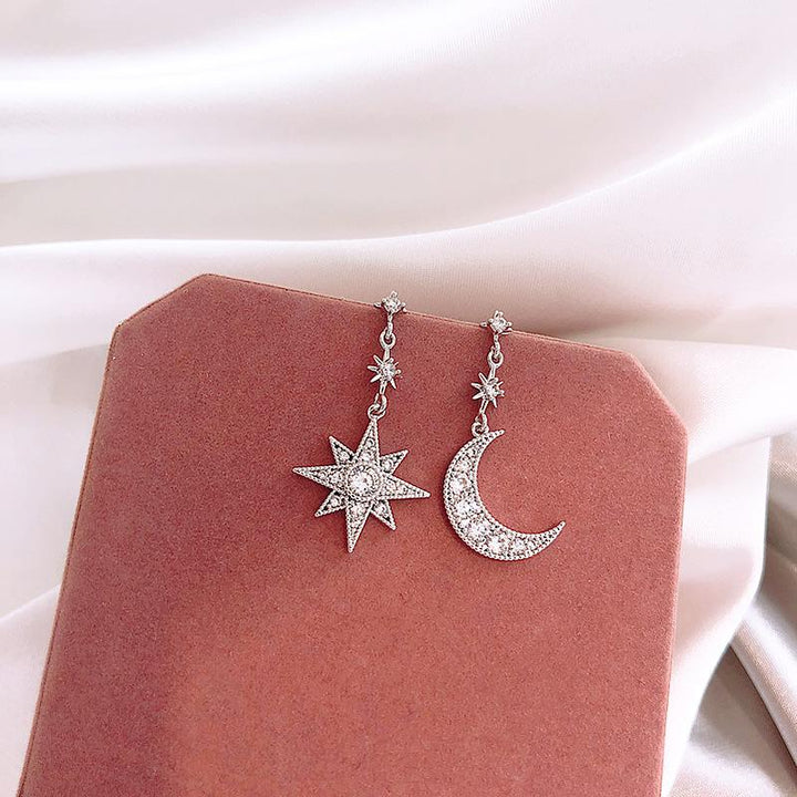 Une paire de boucles d'oreille dépareillées pendantes avec une lune et une étoile en strass - Femme. Un design original et lumineux en cristal et alliage de zinc.