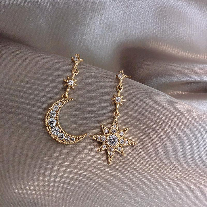 Boucles d'oreille pendantes dépareillées avec lune et étoile en strass - Femme. Un duo harmonieux de cristal et d'alliage de zinc pour briller de mille feux.