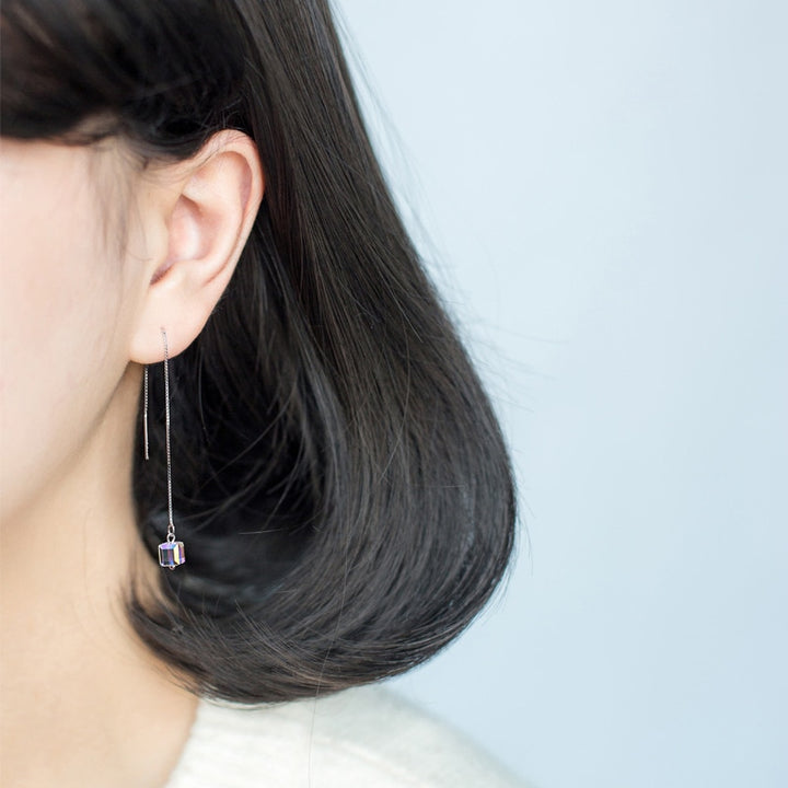 Une femme porte une boucle d'oreille longue à chaîne pendante en argent 925 avec un cristal cubique étincelant. Élégance et modernité pour les femmes sophistiquées.