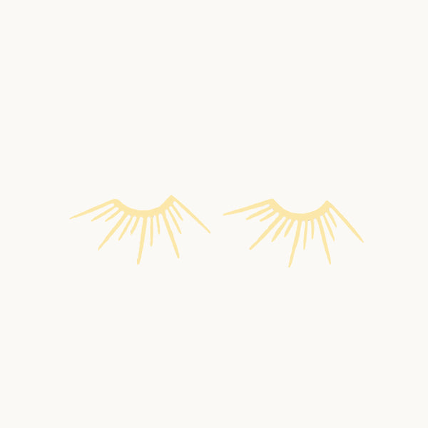 Une paire de boucles d'oreilles est exposée devant un fond beige.   Ce sont des demis soleils plaqué or.