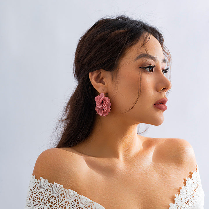 Une femme portant une boucle d'oreille créole fine dorée avec des fleurs en tissu pendantes. Ajoutez une touche florale à votre tenue avec ces boucles d'oreille élégantes et délicates. Parfaites pour les amoureuses de la nature et de la mode.