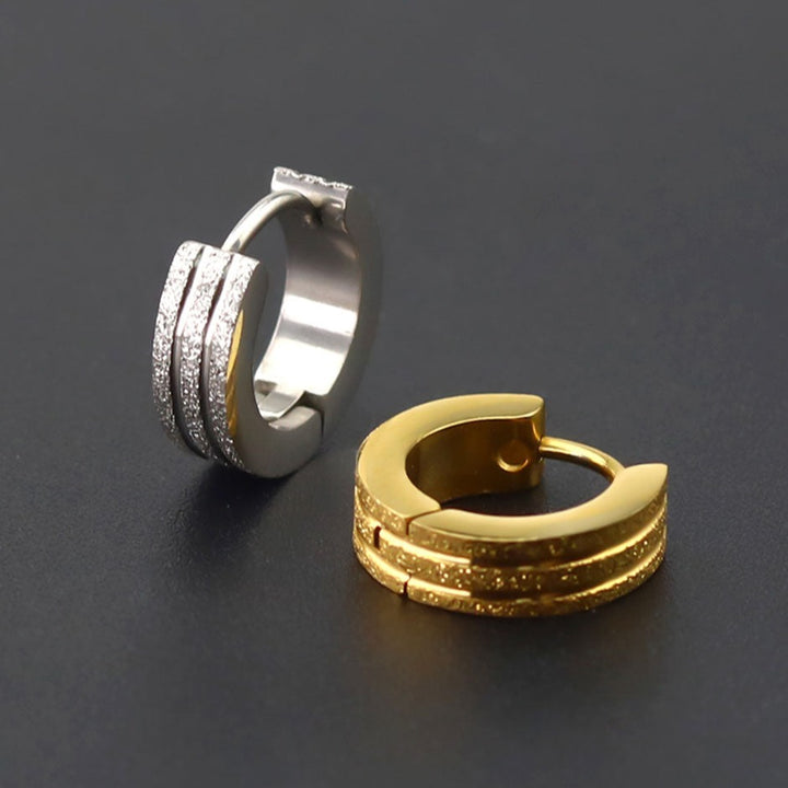 Une paire de boucles d'oreille anneaux pour homme en acier inoxydable avec un mélange unique de trois anneaux pailletés séparés par deux fins anneaux métallisés. Dimensions : 9 x 4 mm. Poids : 3,6 g.