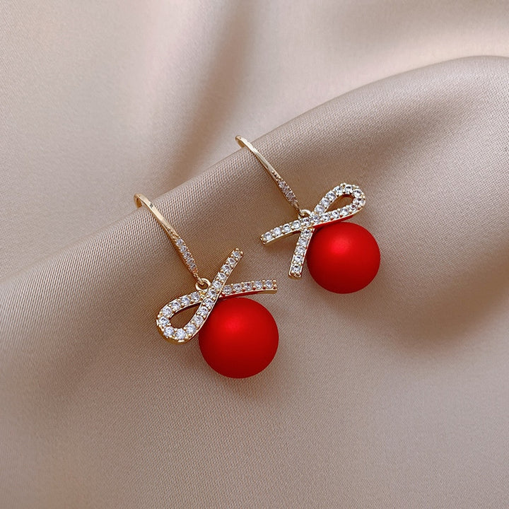 Boucles d'oreille pendantes avec boules rouges et diamants, ornées d'un nœud étincelant en strass. Parfaites pour les fêtes de fin d'année.