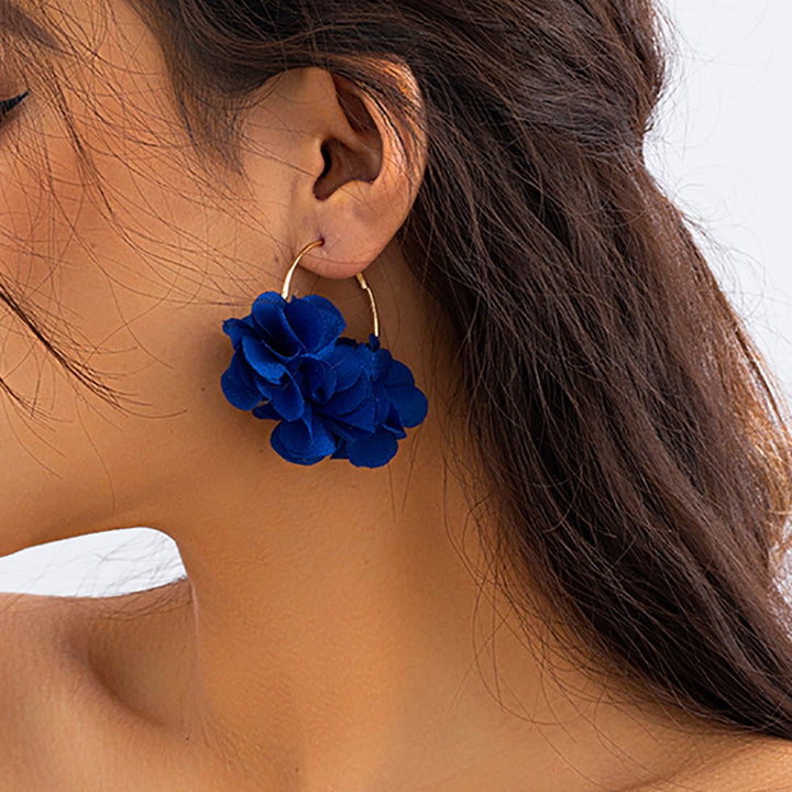 Une femme porte des boucles d'oreille créoles dorées avec de ravissantes fleurs en tissu. Ajoutez une touche florale à votre tenue avec ces bijoux délicats et élégants. Disponibles en six couleurs séduisantes. Parfait pour les amoureuses de la nature et de la mode.