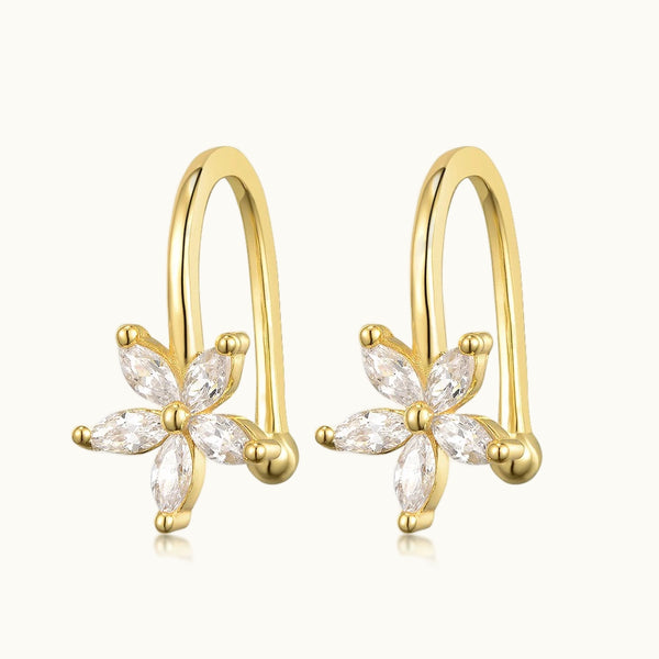 Une paire de boucles d'oreille pour cartilage est sur un fond beige. C'est un anneau clip sans trou. Les boucles sont dorées avec une fleur en diamant. 
