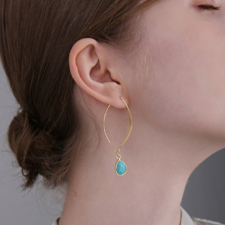 Une femme aux yeux fermés portant une boucle d'oreille pendante ovale en pierre naturelle goutte - Femme. Un design élégant en alliage de zinc doré avec une touche d'authenticité et de mystère.