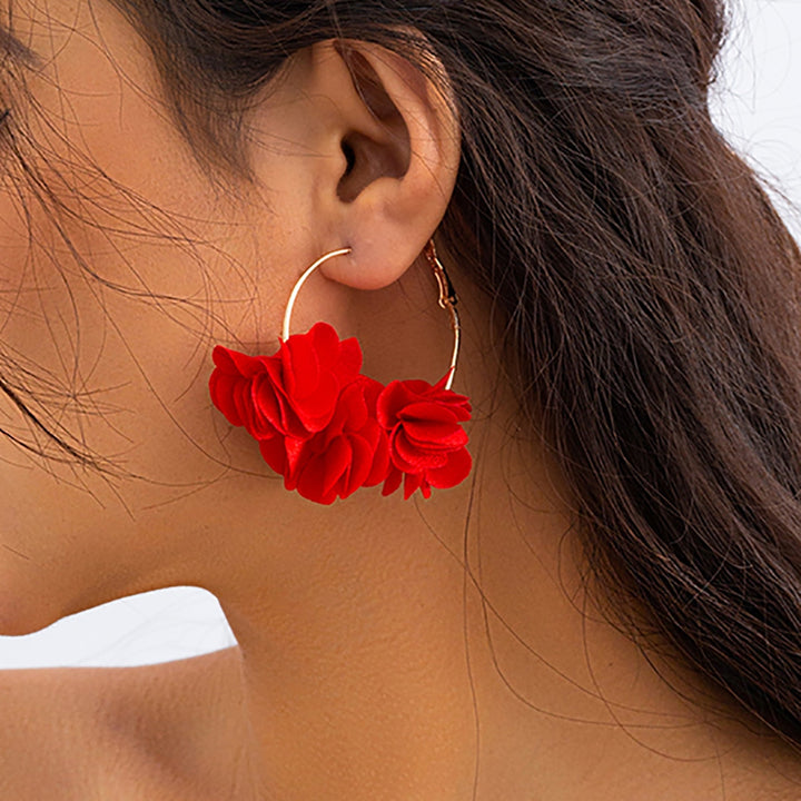 Une femme portant des boucles d'oreille créoles dorées avec de ravissantes fleurs en tissu. Ajoutez une note délicatement féminine à votre tenue avec ces bijoux élégants et légers. Parfait pour les amoureuses de la nature et de la mode.