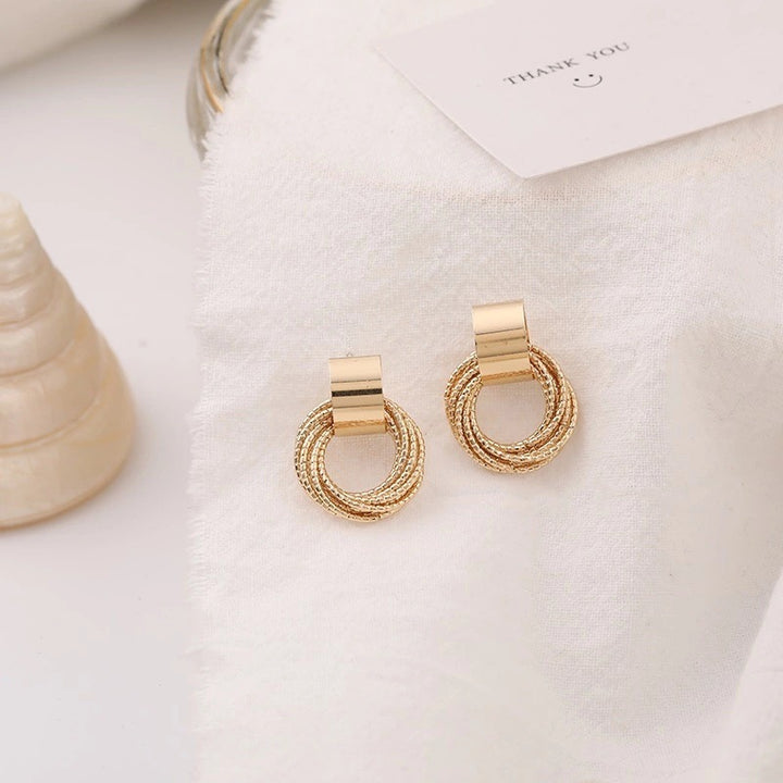 Boucle d'oreille ronde multi anneaux torsadés - Femme, en alliage de zinc. Élégantes boucles d'oreille dorées avec un design fascinant de multiples anneaux torsadés. Dimensions : 2,5 x 2 cm. Poids : 8,2 g.