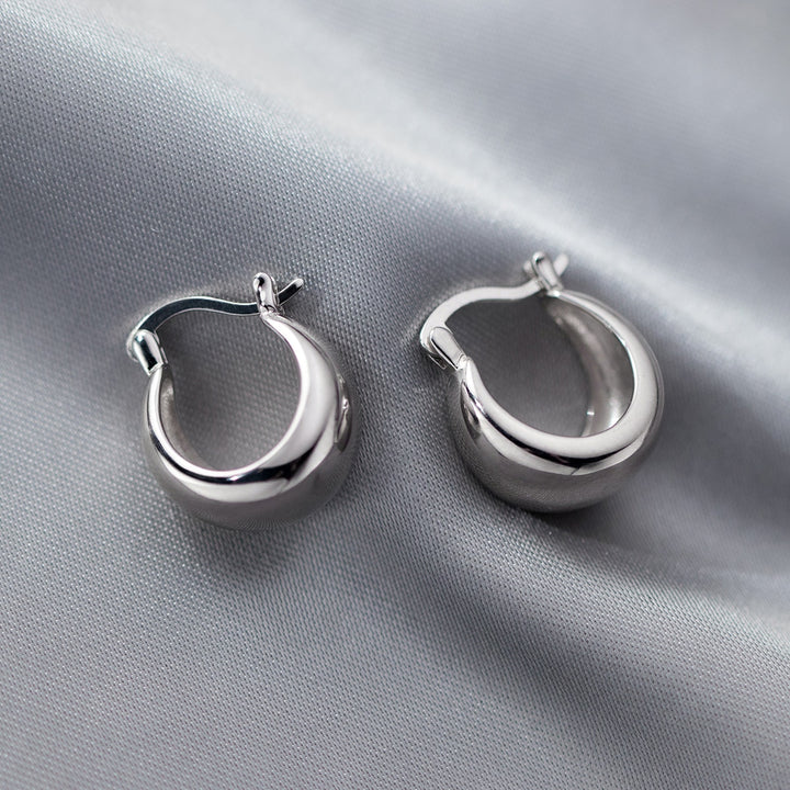 Boucle d'oreille anneau large épais en argent 925, design distinctif avec anneau évasé et extrémités plus minces encadrant un centre plus épais, tige ondulée pour une touche contemporaine. Simplicité et sophistication pour un style classique et moderne. 4g, 1,7 x 0,9 cm.