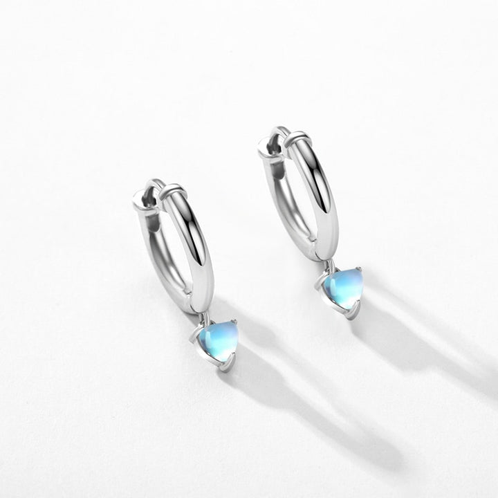 Une paire de boucles d'oreilles en argent 925 avec un anneau en forme de cœur et une pierre de lune bleue. Élégance discrète pour les amatrices d'originalité.