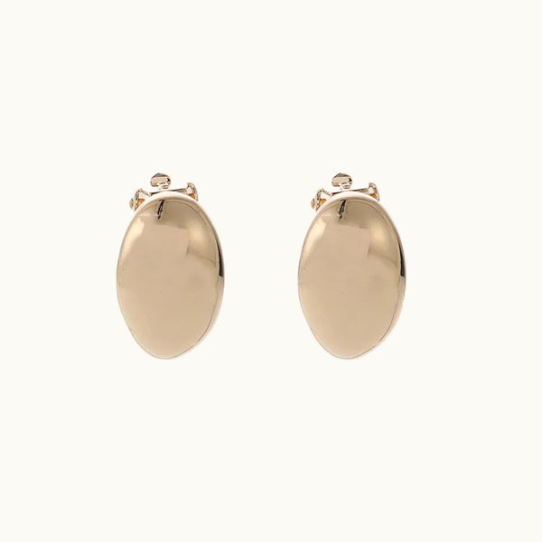 Une paire de boucles d'oreille en forme de gouttes dorées est sur un fond beige. Elles sont à clip, sans trou. 