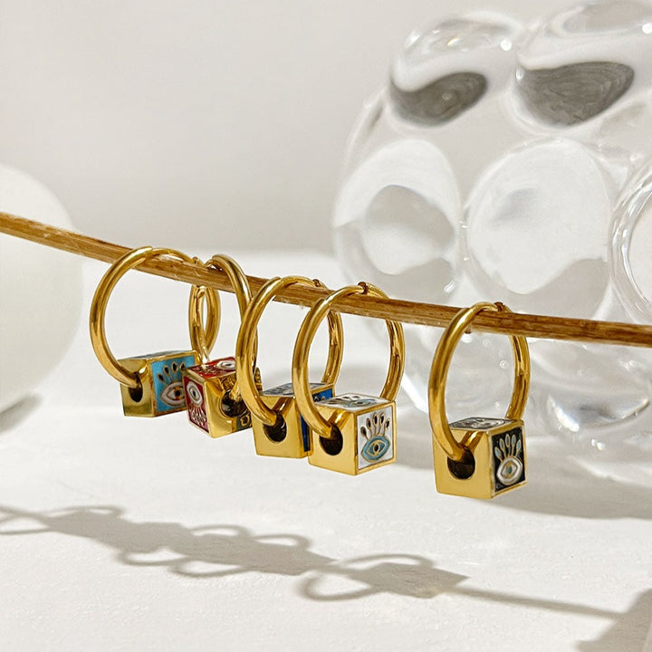 Un groupe de bagues en or avec des motifs, des boucles d'oreille créoles en acier inoxydable plaqué or 18K avec des cubes colorés ornés d'un œil bohème, disponibles en cinq coloris vibrants pour un look élégant et tendance.