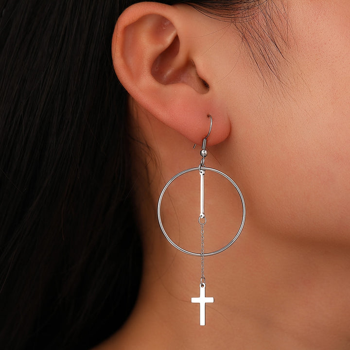 Une femme portant des boucles d'oreilles créoles en argent avec une chaîne et une croix pendante.