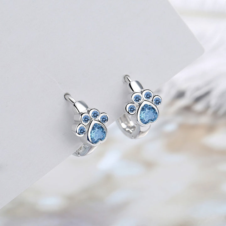 Boucle d'oreille créole patte de chat diamant bleu - Enfant: des boucles d'oreille argentées avec des empreintes de patte de chat et des diamants bleu ciel, parfaites pour les petites filles amoureuses des animaux.