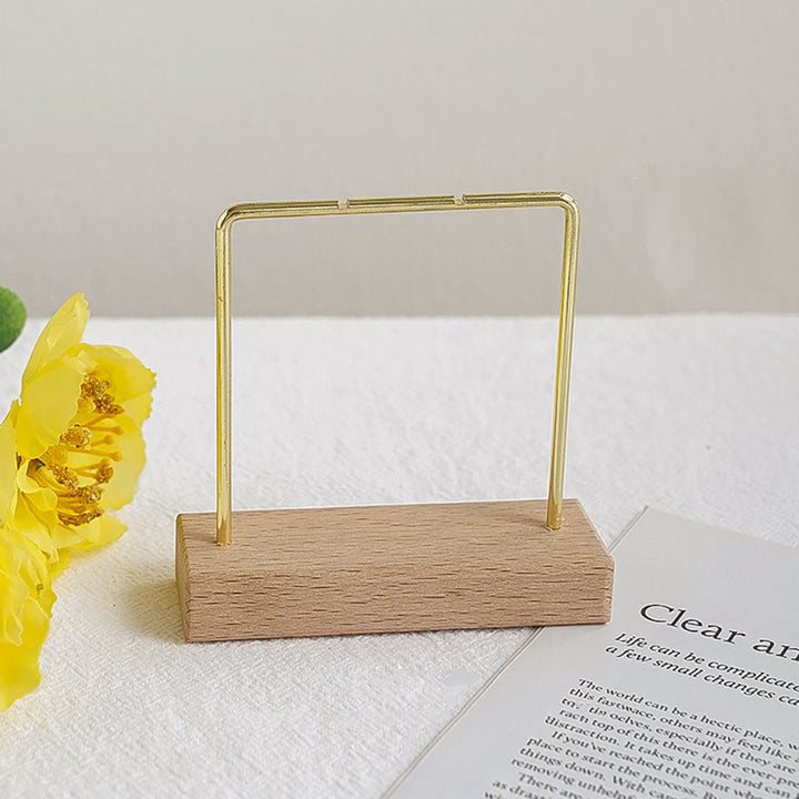 Un présentoir en bois avec une fleur jaune à côté d'un morceau de papier. Présentoir support boucles d'oreille bois métal doré.