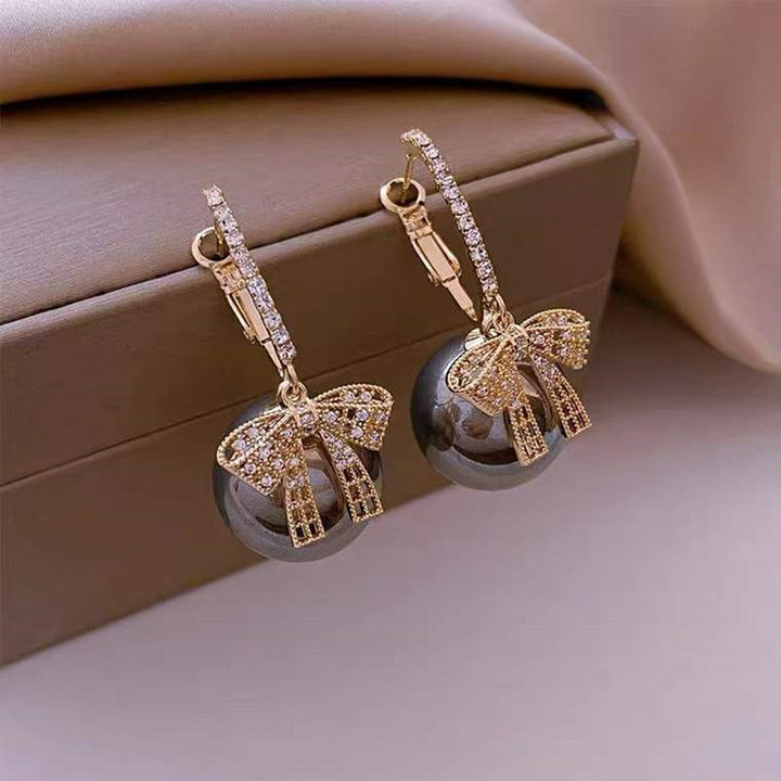 Une paire de boucles d'oreille dormeuses avec un noeud strass et une boule de Noël pendante - Femme. Un joyau festif pour illuminer votre look pendant les fêtes.